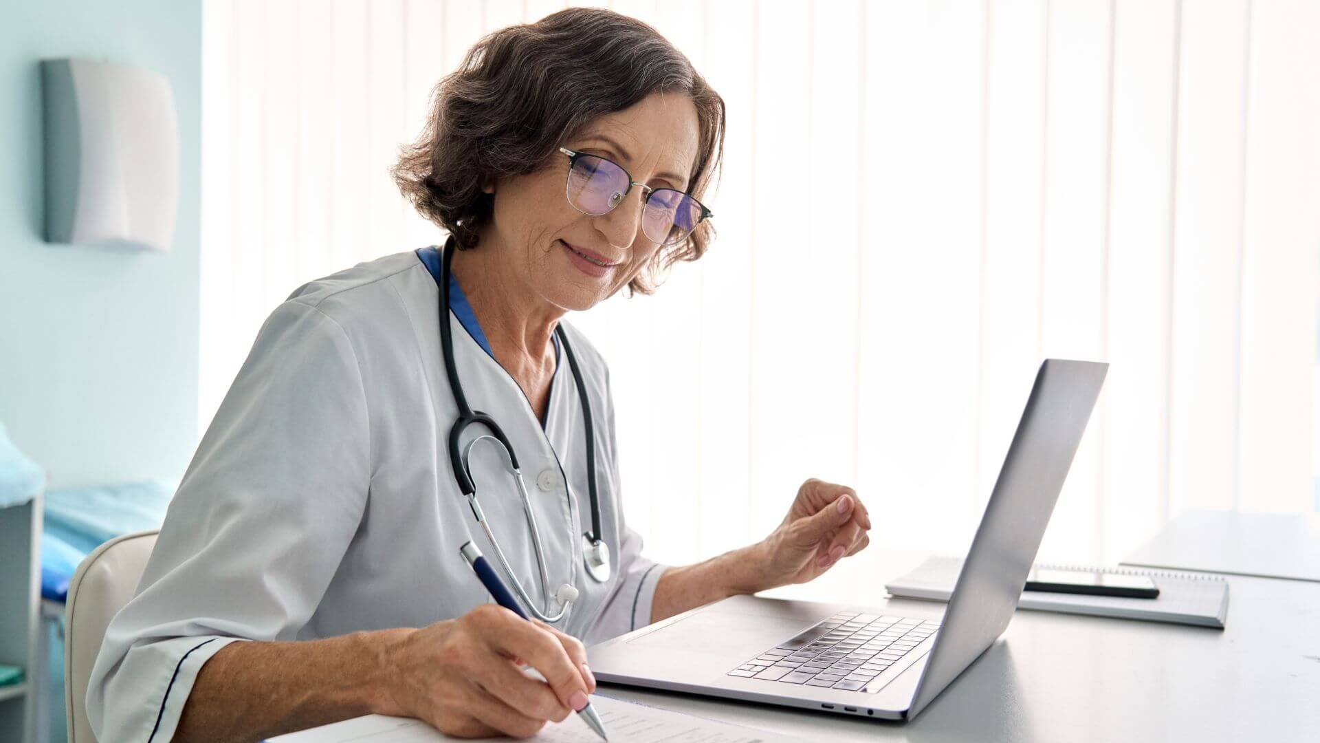 Eine Ärztin arbeitet in der Telemedizin und macht sich Notizen aus einer Videosprechstunde