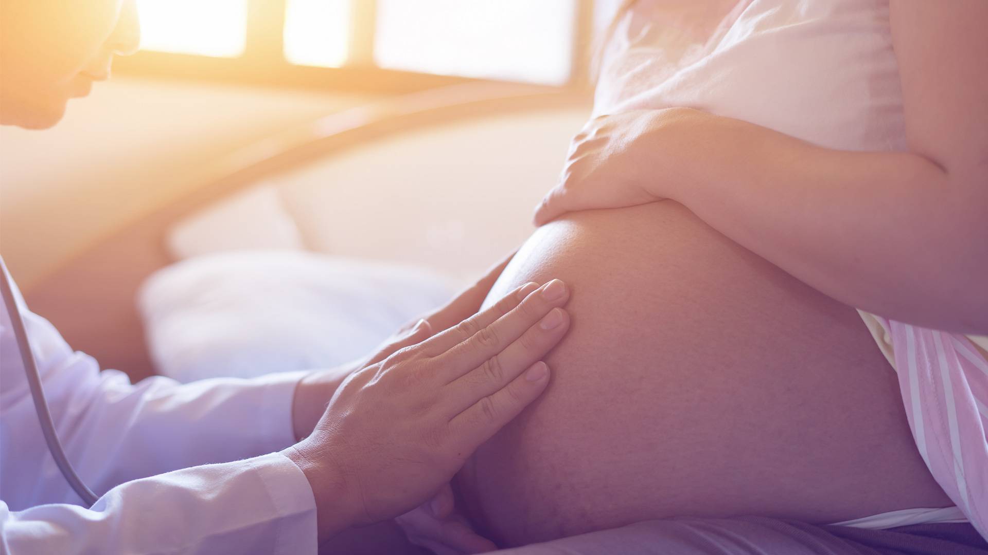 Ärztin tastet den Bauch einer hochschwangeren Kollegin ab