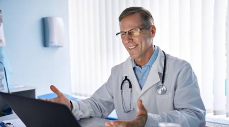 Arzt sitzt dank funktionierender Praxissoftware lächelnd vor dem Laptop