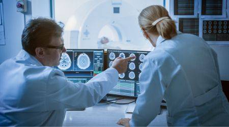 Arzt und Ärztin werten in einem Kontrollraum das CT eines Patienten aus