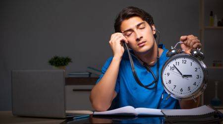 erschöpfter Arzt mit Stethoskop und Wecker in der Hand