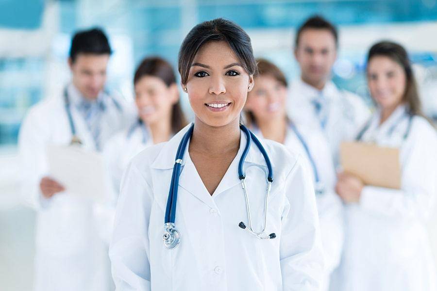 Eine zufriedene Ärztin steht lächelnd vor einer Gruppe von Kollegen