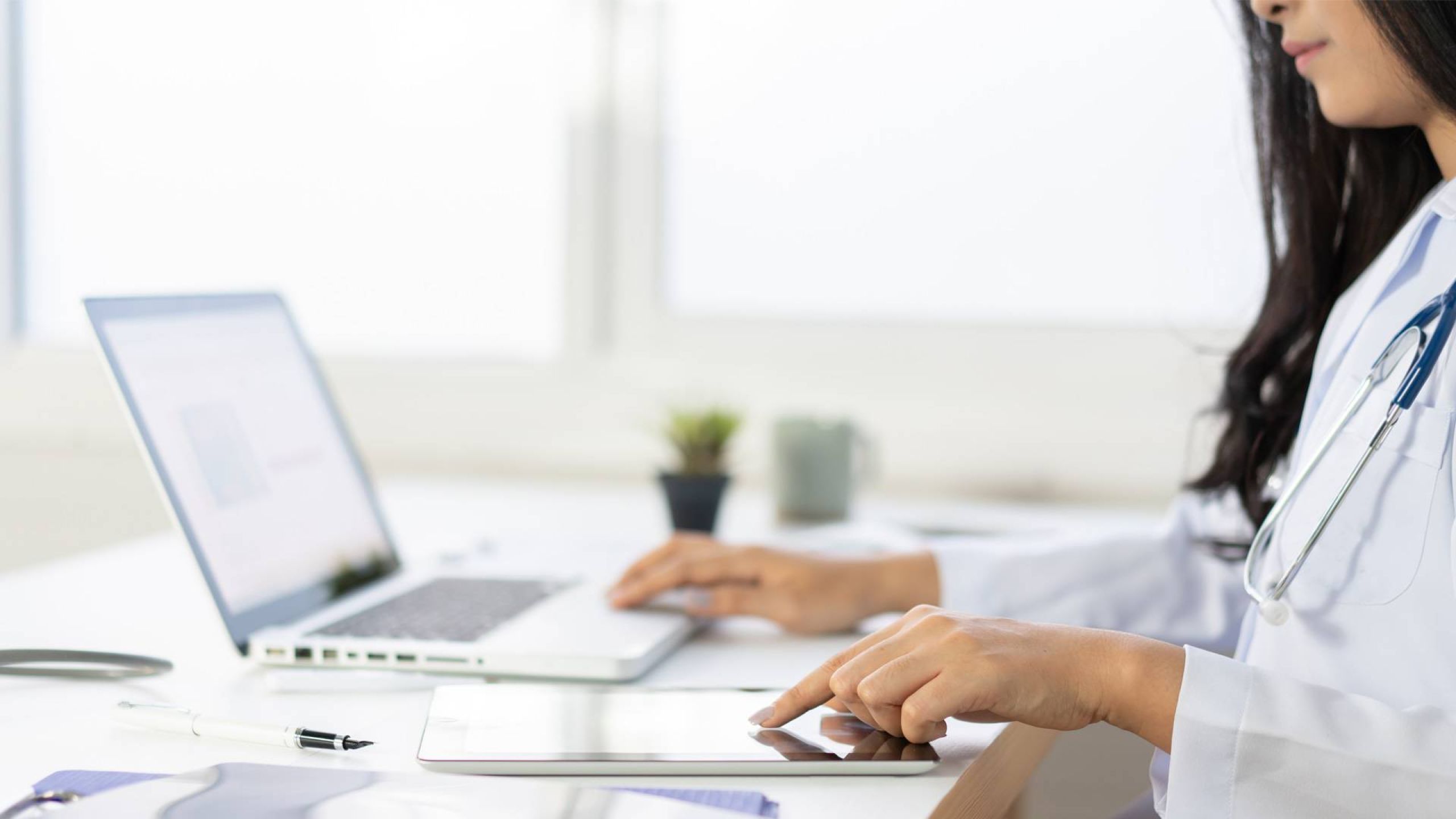 Die richtige Praxissoftware ermöglicht Ärzten ein multimediales Arbeiten Junge Ärztin arbeitet unter Einsatz von Praxissoftware am Laptop und Macbook