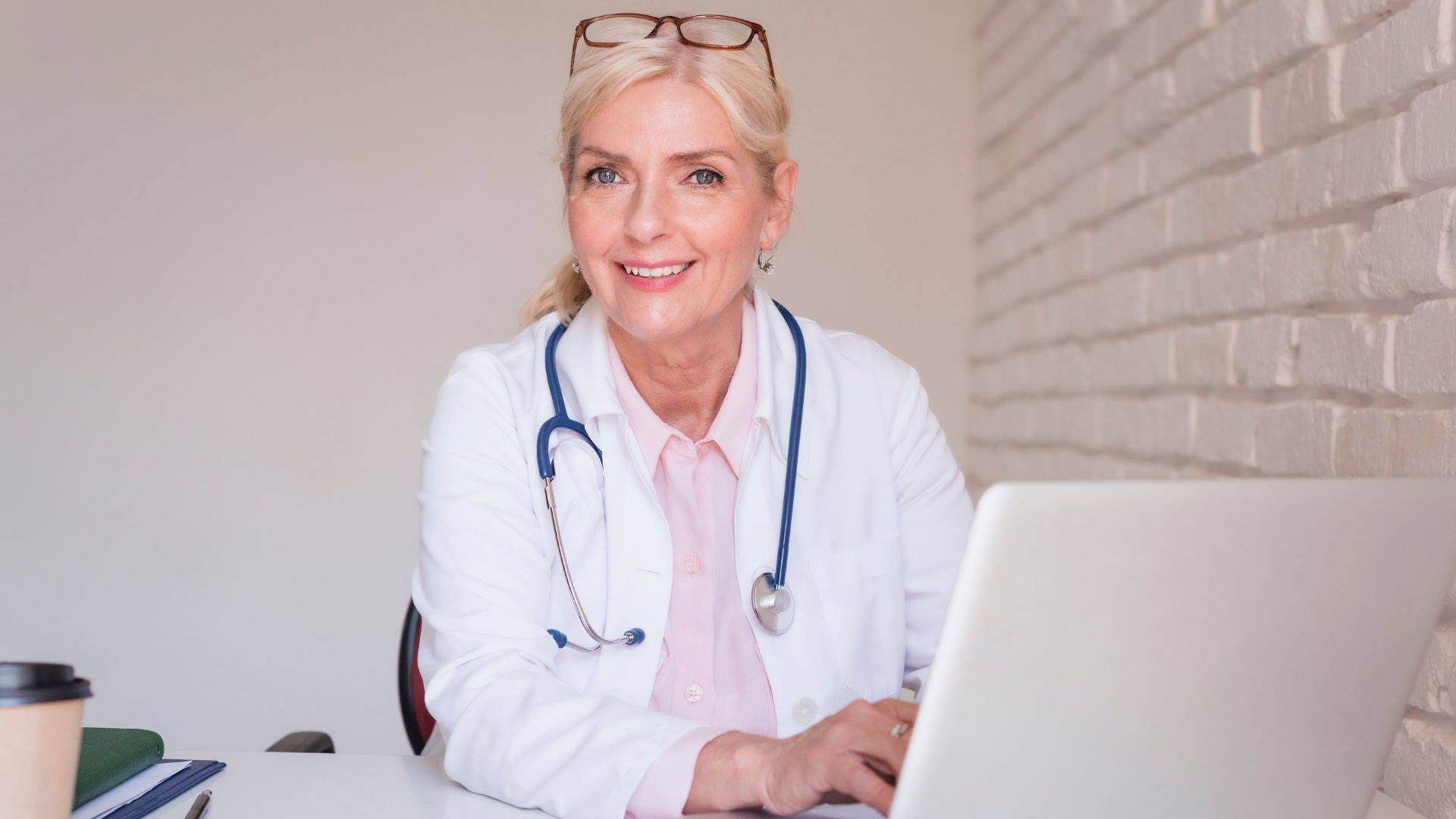 Eine Oberärztin mit Stethoskop sitzt mit einem Laptop an einem Schreibtisch