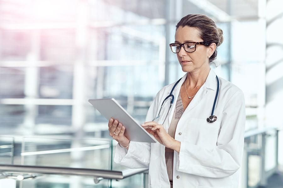 Eine Ärztin, die in einer medizinischen Einrichtung angestellt ist, liest auf ihrem Tablet die Antworten der HiPo Ärztevermittlung auf die FAQs