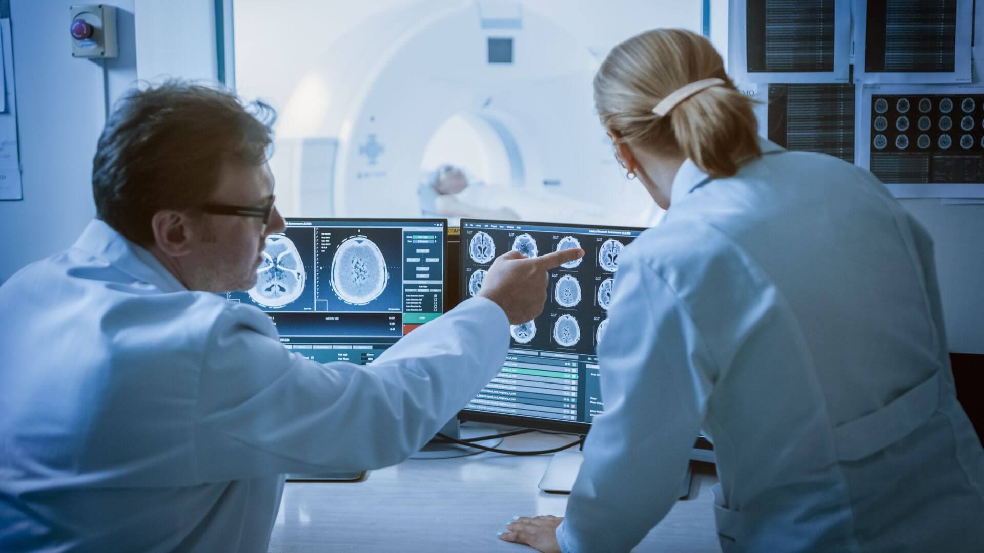 Zwei Ärzte führen, geschützt von Strahlen, eine CT-Untersuchung bei einem Patienten durch 