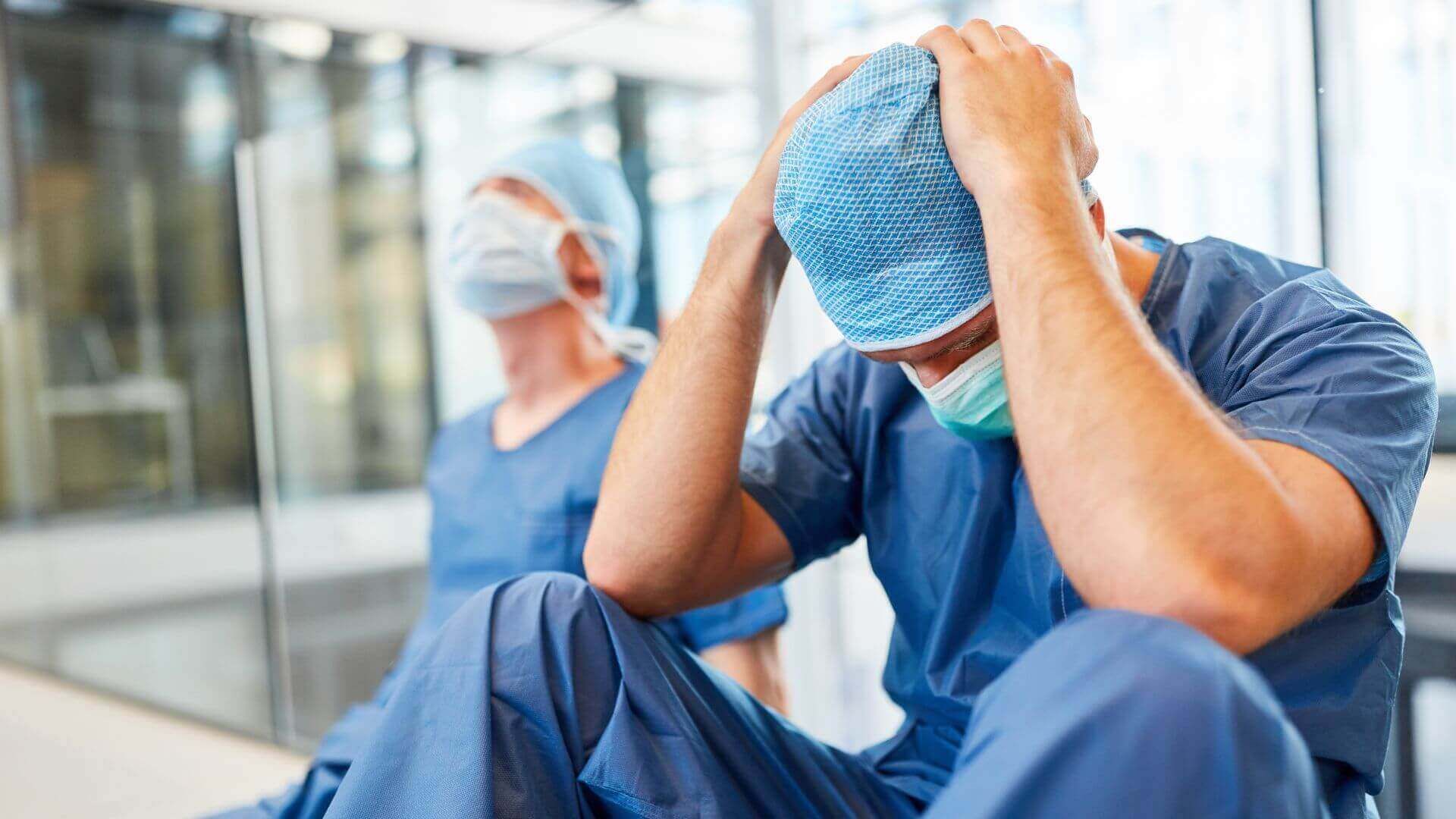 Zwei Chirurgen sitzen psychisch überlastet auf dem Boden in einer Klinik