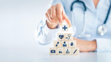 Ein Arzt baut eine Pyramide aus Holzwürfeln, die unterschiedliche Symbole aus der Medizin darstellen