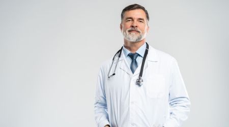 Klischeehaft aussehender Arzt steht selbstbewusst vor weißer Wand