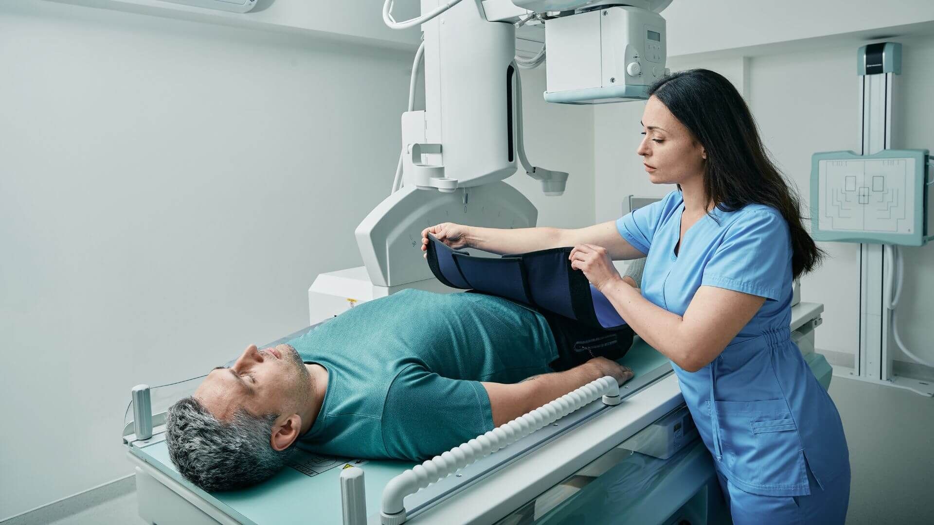 Eine Assistenzärztin legt einem Patienten einen Röntgen Strahlenschutz vor der Untersuchung um